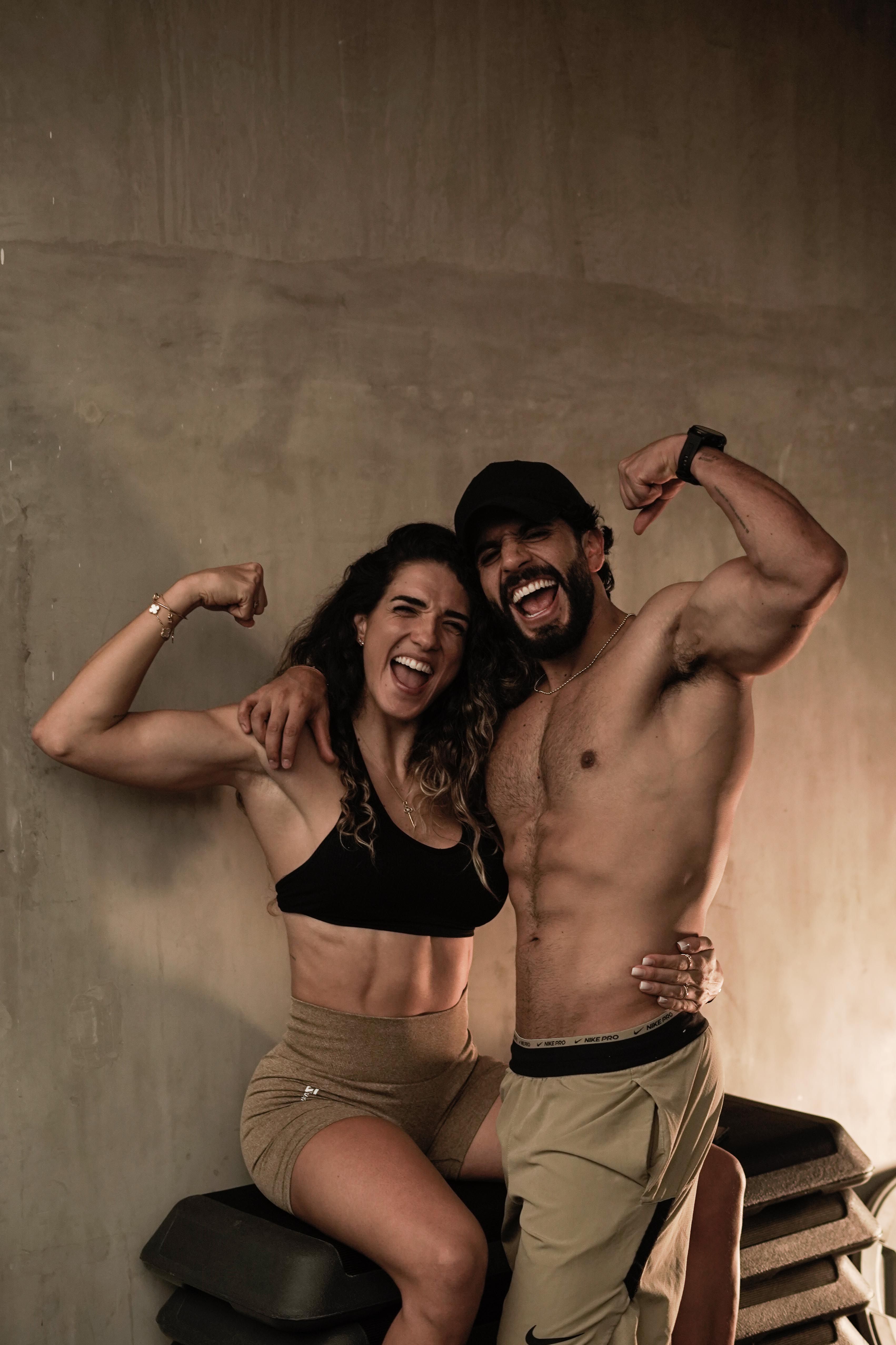 Pareja flexionando los brazos y sonriendo después de entrenar